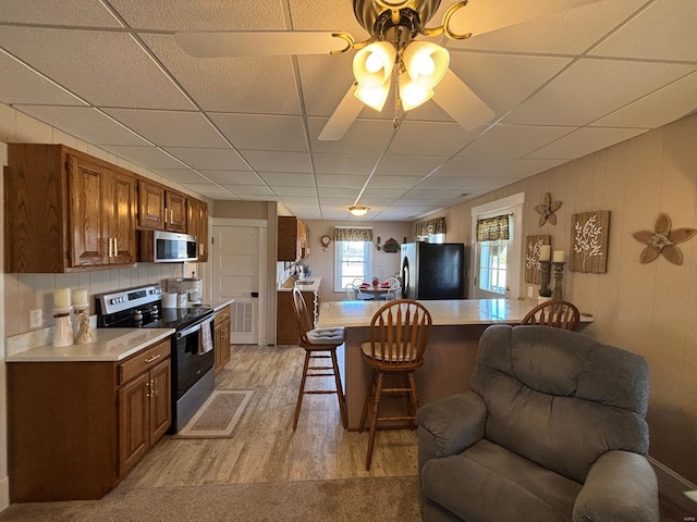 kitchen featuring light countertops, a kitchen breakfast bar, brown cabinets, light wood-type flooring, and stainless steel appliances