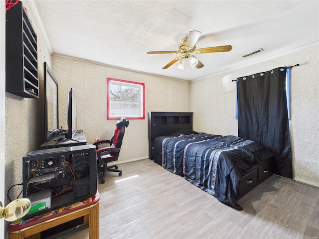 bedroom featuring a textured ceiling, visible vents, ornamental molding, wood finished floors, and a textured wall