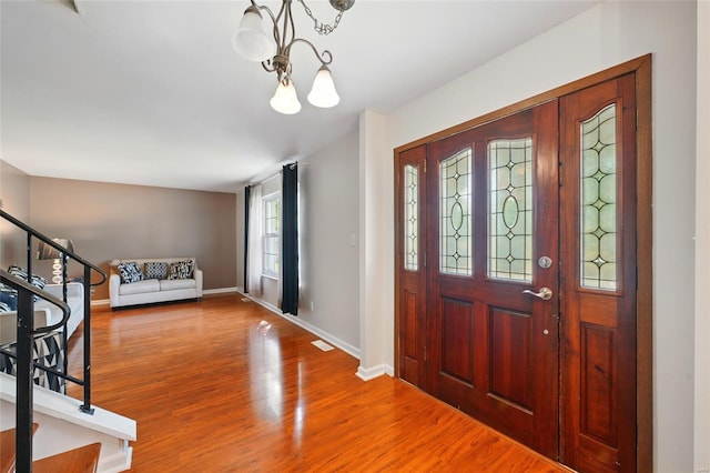 entrance foyer with a notable chandelier, baseboards, wood finished floors, visible vents, and stairway
