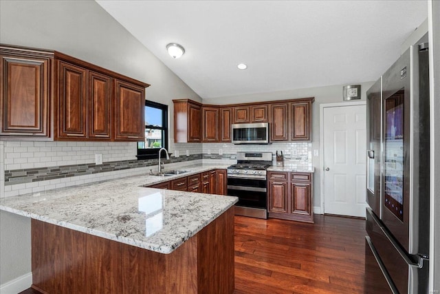 kitchen with dark wood finished floors, a peninsula, vaulted ceiling, appliances with stainless steel finishes, and a sink