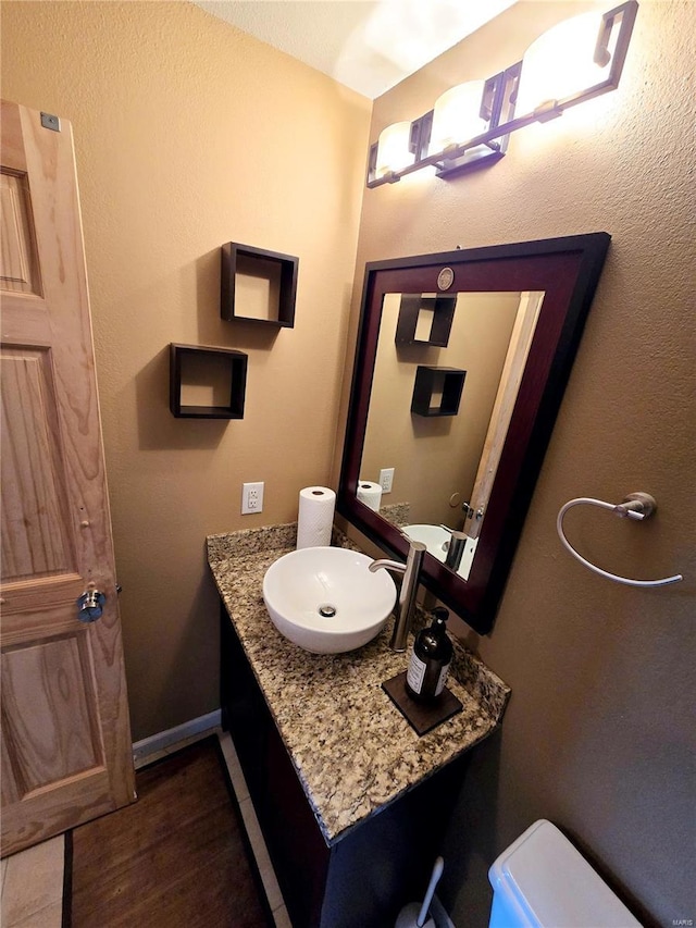bathroom with toilet, vanity, and wood finished floors
