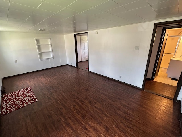 empty room with baseboards, built in shelves, and wood finished floors