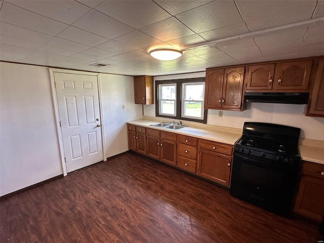 kitchen featuring light countertops, under cabinet range hood, a sink, dark wood-style floors, and black gas range