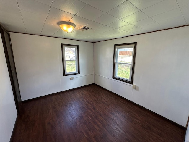 unfurnished room featuring visible vents, dark wood-type flooring, and a healthy amount of sunlight