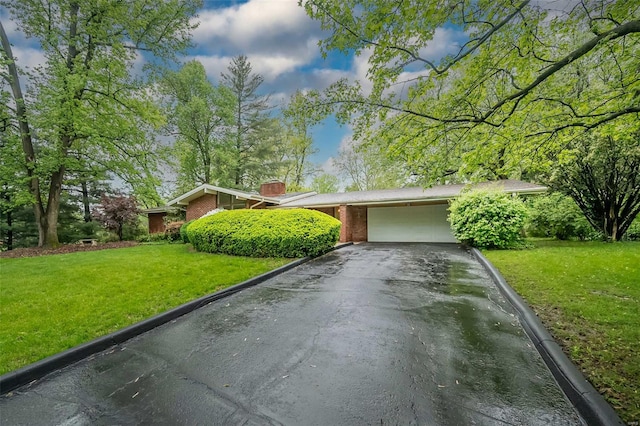 view of front facade with a garage, a chimney, a front lawn, brick siding, and driveway