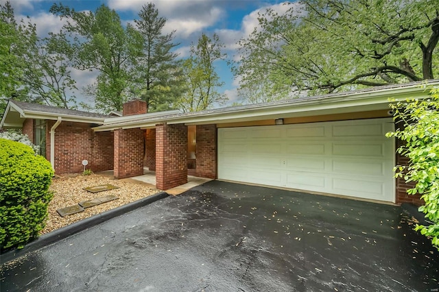 view of front of property featuring an attached garage, a chimney, brick siding, and driveway