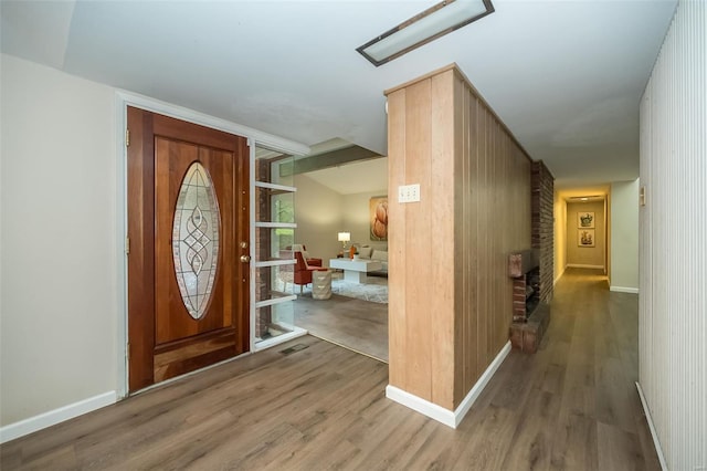 entrance foyer with baseboards, a brick fireplace, and wood finished floors