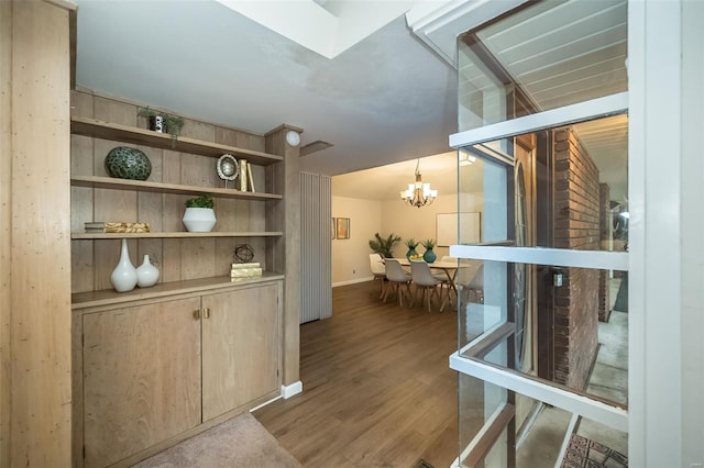 hall with wood finished floors, baseboards, and a notable chandelier