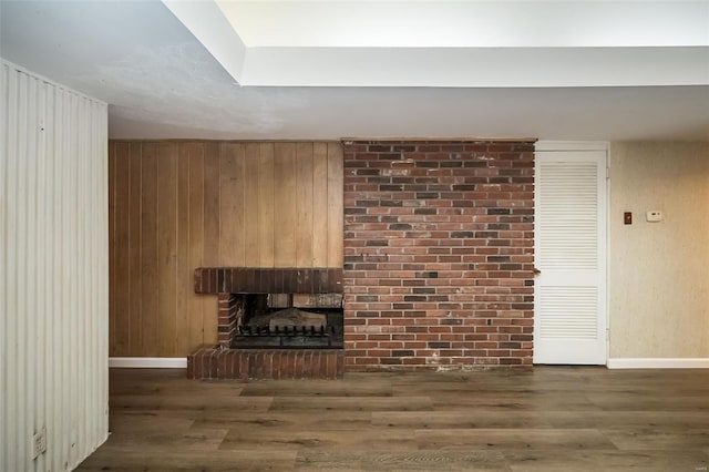 unfurnished living room with a fireplace, wood walls, baseboards, and wood finished floors
