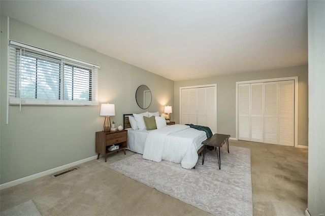 bedroom featuring baseboards, carpet floors, visible vents, and two closets