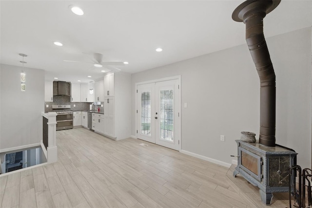 unfurnished living room featuring ceiling fan, a wealth of natural light, a wood stove, and baseboards