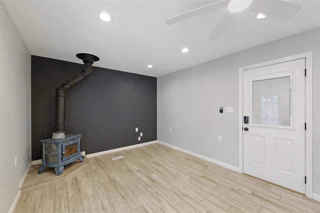 unfurnished living room featuring light wood-style floors, a wood stove, baseboards, and ceiling fan