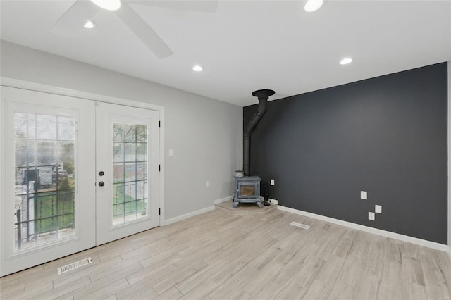 unfurnished living room with french doors, visible vents, a wood stove, and light wood-style flooring