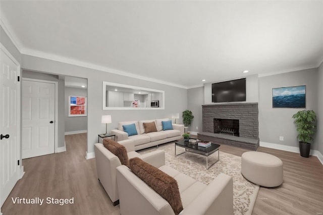 living room featuring light wood-style flooring, ornamental molding, baseboards, and a stone fireplace