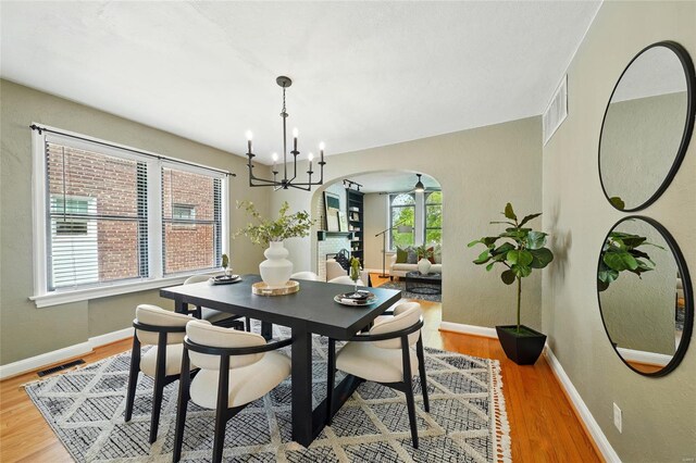 dining space featuring an inviting chandelier, arched walkways, baseboards, wood finished floors, and visible vents