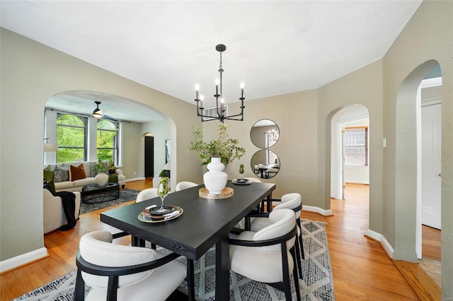 dining space featuring light wood-type flooring, arched walkways, a notable chandelier, and a healthy amount of sunlight