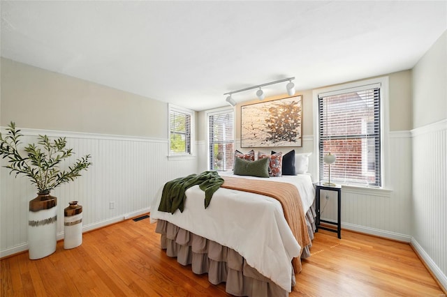 bedroom featuring light wood-style floors, rail lighting, and a wainscoted wall