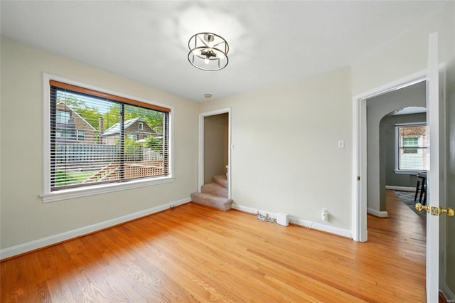 unfurnished room with stairs, arched walkways, baseboards, and wood finished floors