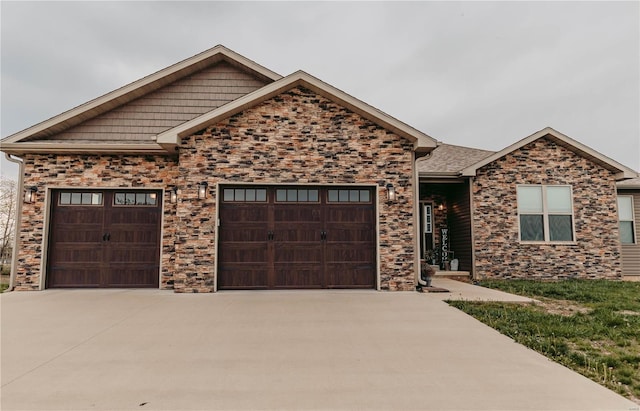 view of front of property featuring an attached garage, stone siding, and concrete driveway
