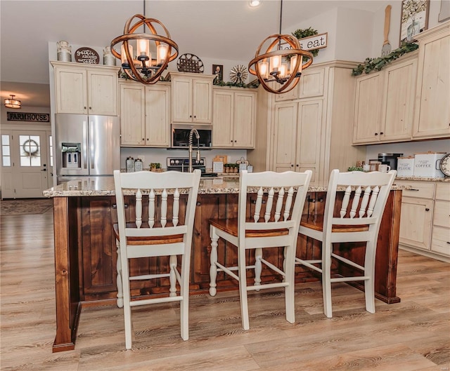 kitchen featuring light wood finished floors, a center island with sink, pendant lighting, a chandelier, and appliances with stainless steel finishes