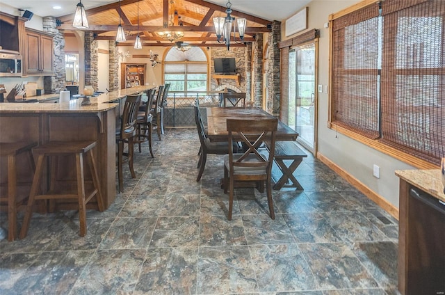 dining space with an inviting chandelier, decorative columns, vaulted ceiling with beams, stone finish floor, and baseboards