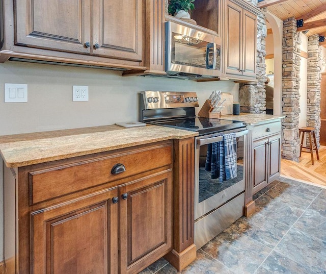 kitchen featuring light stone countertops, wood ceiling, stone finish floor, appliances with stainless steel finishes, and brown cabinets