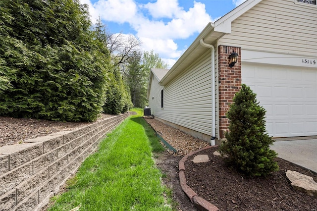 view of side of property featuring a yard, brick siding, an attached garage, and cooling unit