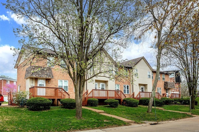 view of front of house featuring brick siding, a deck, and a front lawn