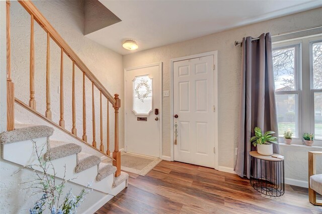 entryway with a textured wall, baseboards, stairs, and wood finished floors