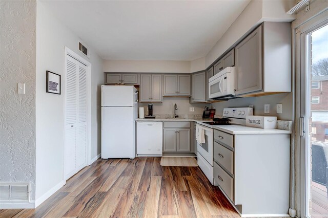 kitchen with white appliances, gray cabinetry, a sink, visible vents, and wood finished floors