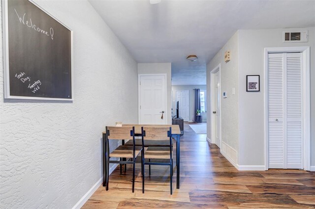 hall with wood finished floors, a textured wall, baseboards, and visible vents