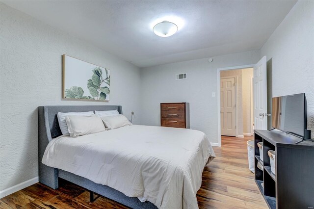 bedroom featuring baseboards, visible vents, wood finished floors, and a textured wall