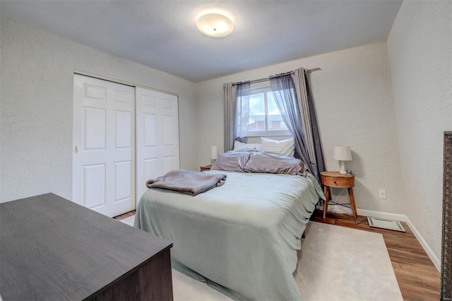 bedroom with baseboards, light wood-type flooring, and a textured wall