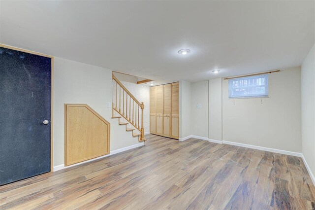 below grade area featuring light wood-style flooring, baseboards, and stairway