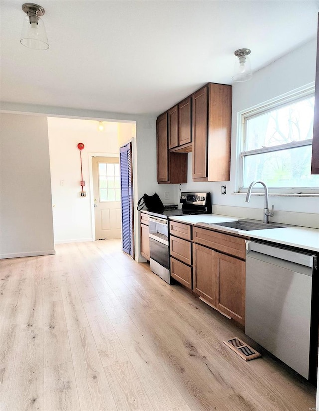 kitchen featuring a sink, stainless steel appliances, visible vents, light wood finished floors, and light countertops