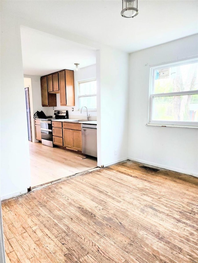 kitchen featuring stainless steel dishwasher, a sink, light wood-style floors, light countertops, and electric range