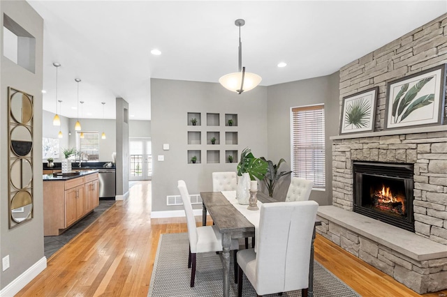 dining room featuring visible vents, a stone fireplace, light wood-style flooring, and baseboards