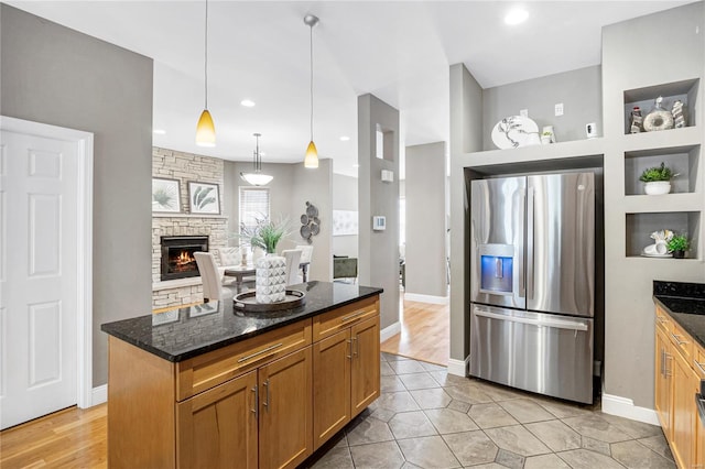 kitchen with dark stone counters, open shelves, a kitchen island, a fireplace, and stainless steel refrigerator with ice dispenser