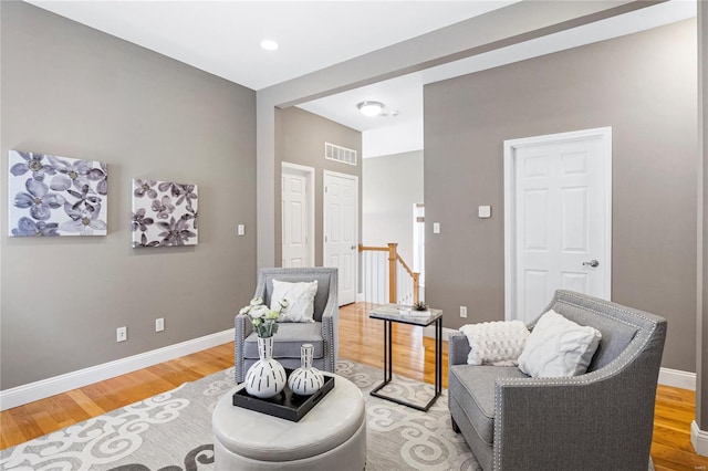 sitting room featuring baseboards, visible vents, an upstairs landing, and light wood-style flooring