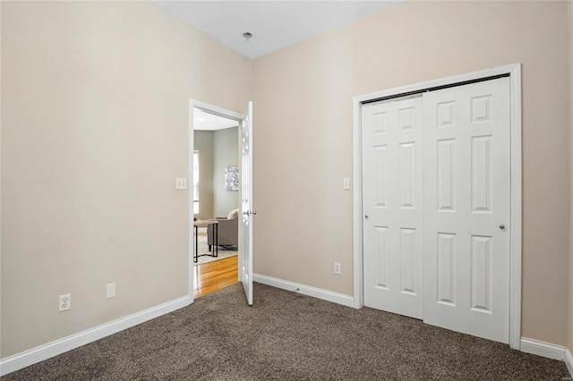 unfurnished bedroom featuring dark carpet, a closet, and baseboards