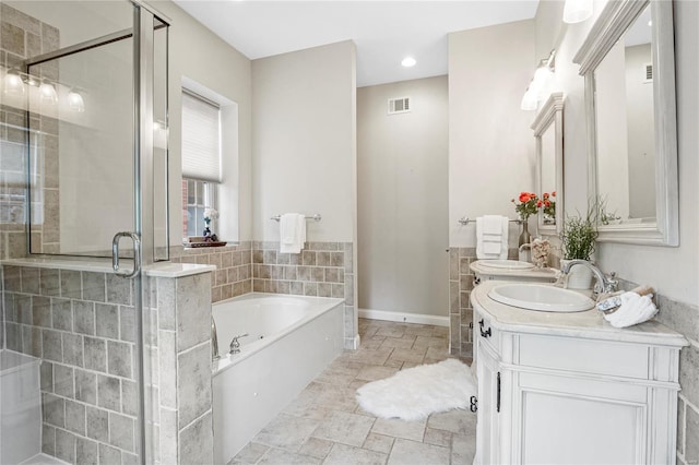 full bathroom featuring a sink, a shower stall, stone tile flooring, visible vents, and a garden tub