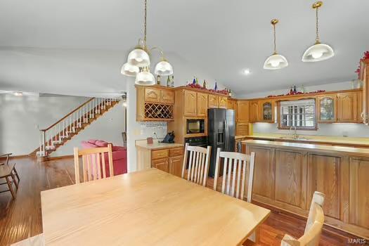 dining room featuring an inviting chandelier, stairs, vaulted ceiling, and wood finished floors