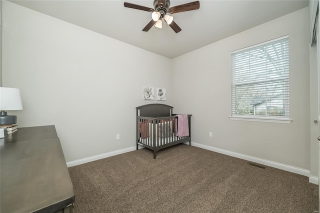 carpeted bedroom featuring a crib, visible vents, baseboards, and a ceiling fan