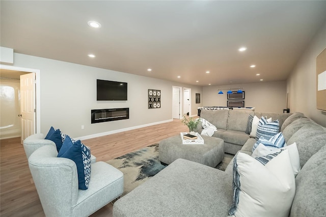 living room with a glass covered fireplace, recessed lighting, baseboards, and wood finished floors