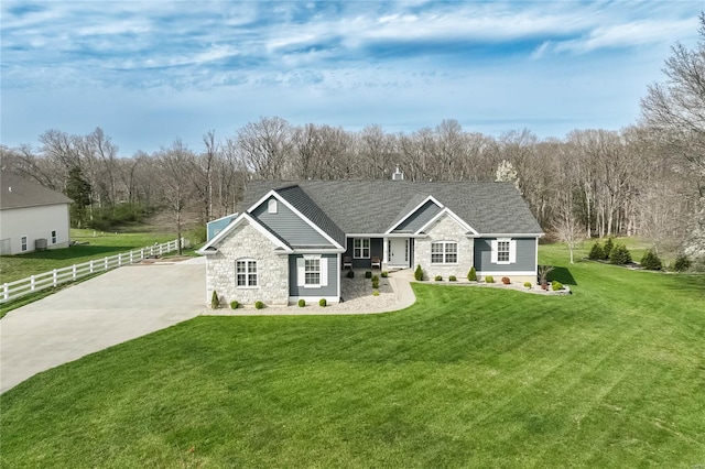 single story home featuring concrete driveway, stone siding, a front yard, fence, and a shingled roof
