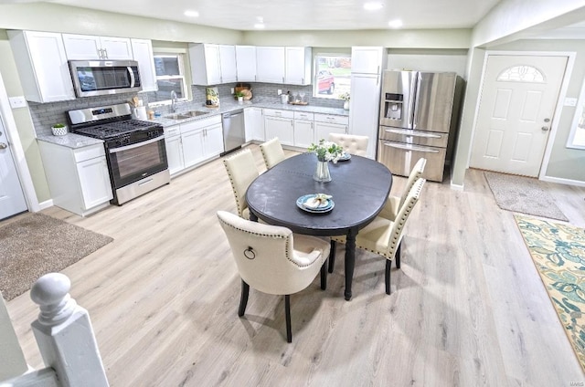 kitchen featuring light wood-type flooring, white cabinets, appliances with stainless steel finishes, a sink, and decorative backsplash
