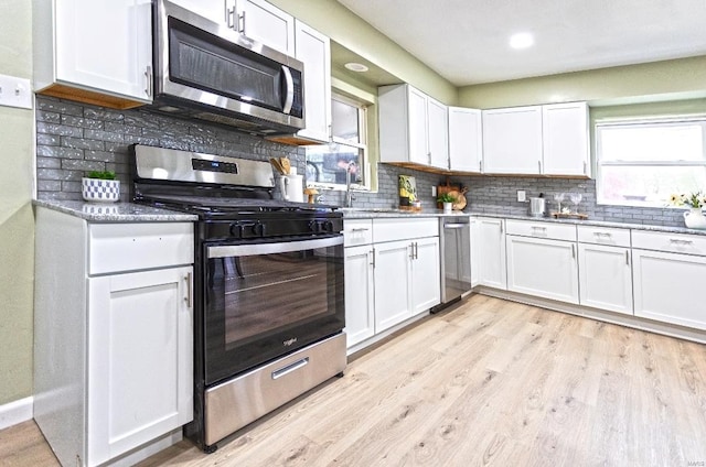 kitchen with light stone counters, white cabinetry, backsplash, light wood-style floors, and stainless steel appliances