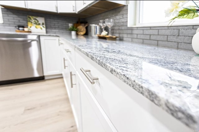 kitchen with light wood-style flooring, white cabinets, light stone counters, dishwasher, and backsplash