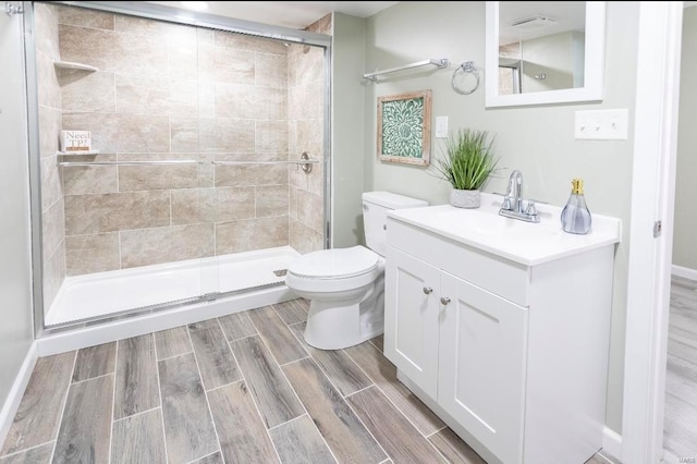 bathroom with a shower stall, vanity, wood tiled floor, and toilet