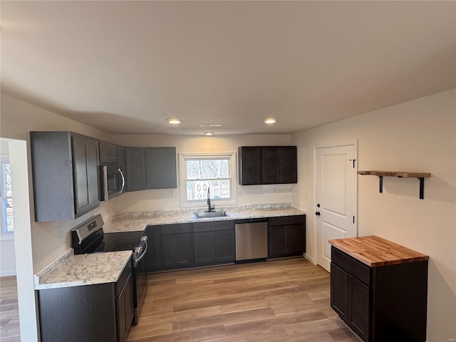 kitchen featuring recessed lighting, open shelves, light wood-style floors, stainless steel appliances, and a sink